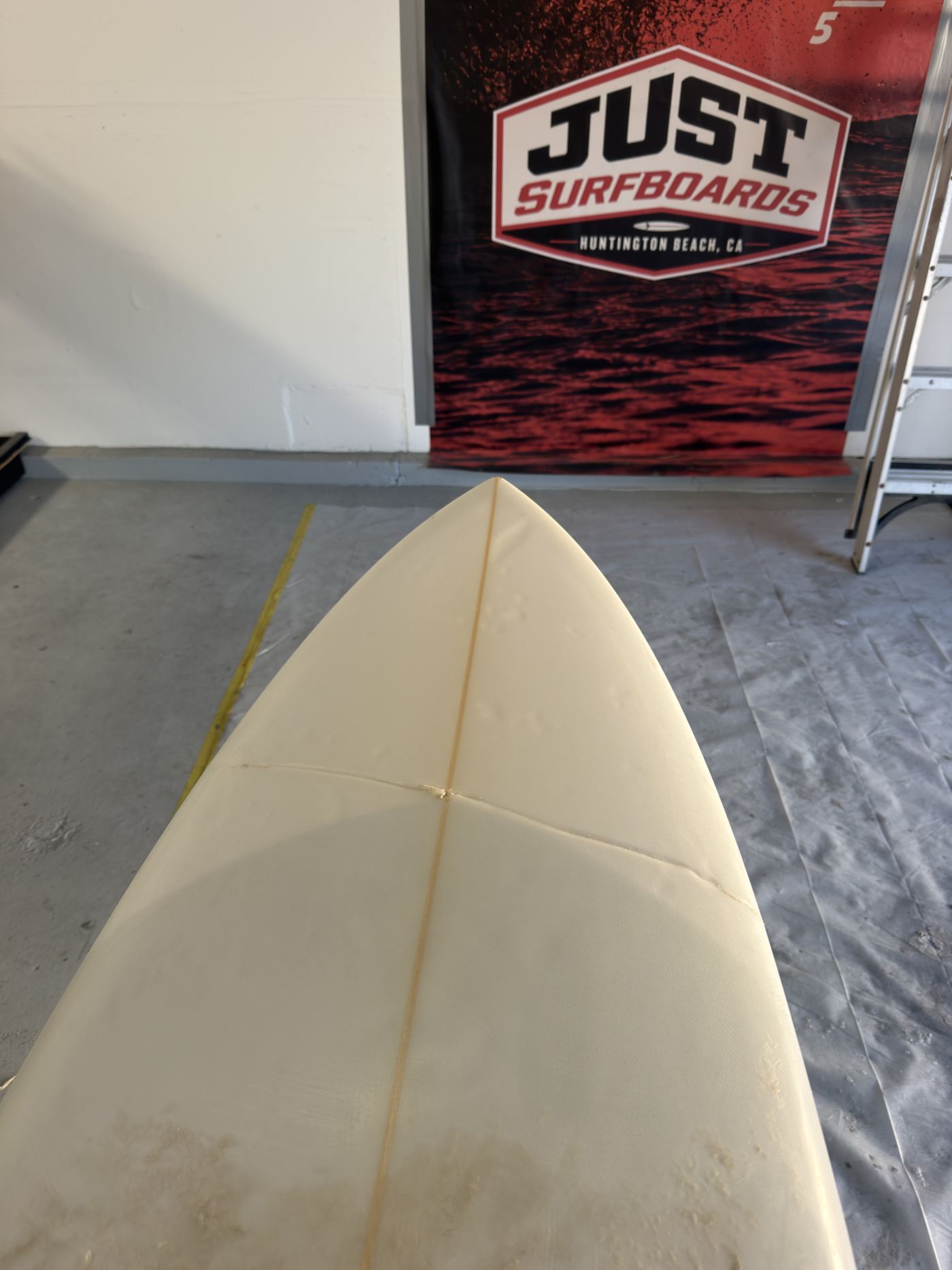 Surfboard with a buckle across the nose in front of the Just Surfboards banner in Huntington Beach