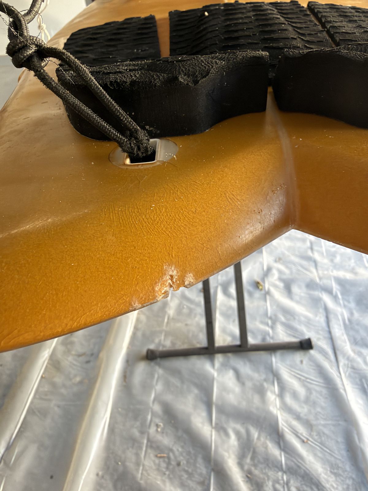Rail ding on the tail of an amber fish surfboard on the repair stand at Just Surfboards in Huntington Beach
